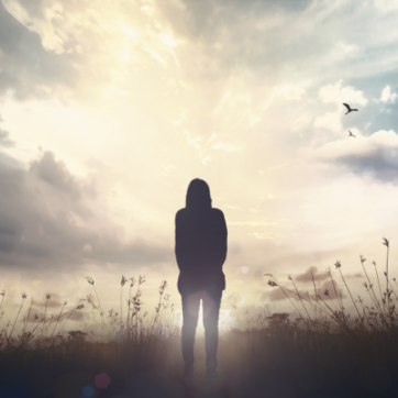 The silhouette of a person looking into the distance while standing in a field facing the sun