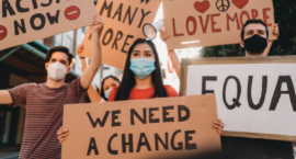 People holding up signs that say: We Need A Change, Act Now, Equal Rights, Love More