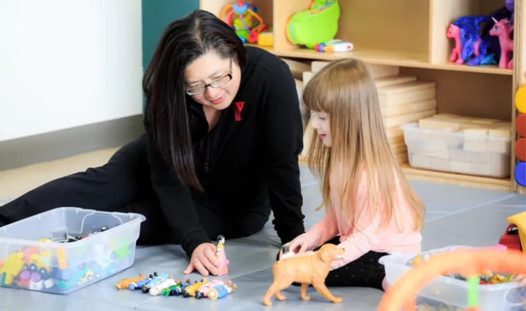 A child care working and a little girl are playing with toys together.