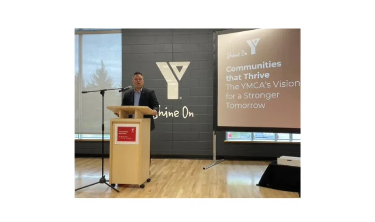 Peter Dinsdale is standing at a podium speaking. There is a screen projected behind him with the words:: Communities that Thrive. The YMCA's Vision for a Stronger Tomorrow