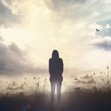The silhouette of a person looking into the distance while standing in a field facing the sun