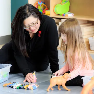 A child care working and a little girl are playing with toys together.
