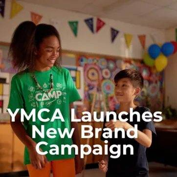 Text: YMCA Launches New Brand Campaign. Image: A girl and a boy are standing inside a child care room smiling at each other.